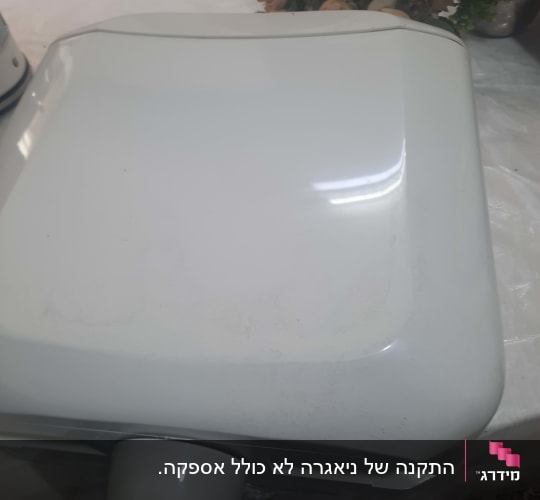 מיכל מים לבן על שולחן עם פרחים ברקע